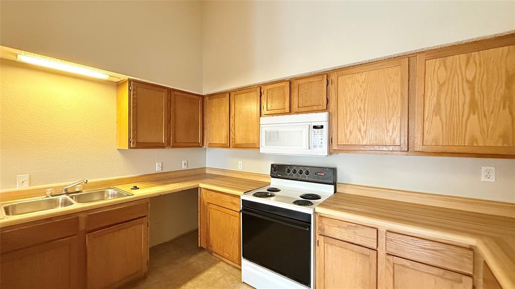 6108 Abrams Road, Unit 125 Dallas, TX 75231 - Photo 7 of 20 Kitchen featuring wood-finish cabinetry, a double basin stainless steel sink, a microwave, and a range oven