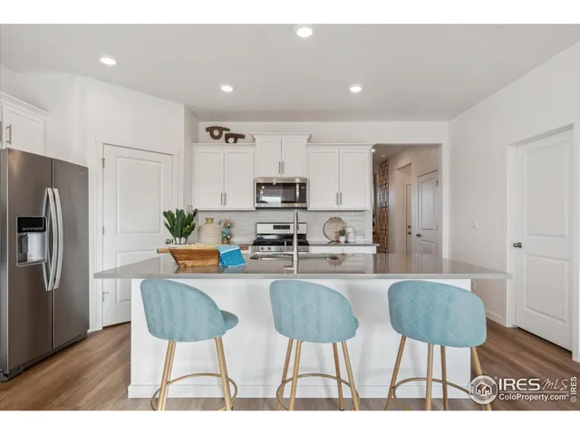a kitchen with stainless steel appliances kitchen island granite countertop a dining table chairs and a refrigerator