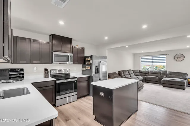 a large white kitchen with stainless steel appliances kitchen island a stove a sink a refrigerator and white cabinets