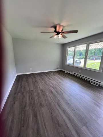 an empty room with wooden floor chandelier fan and windows