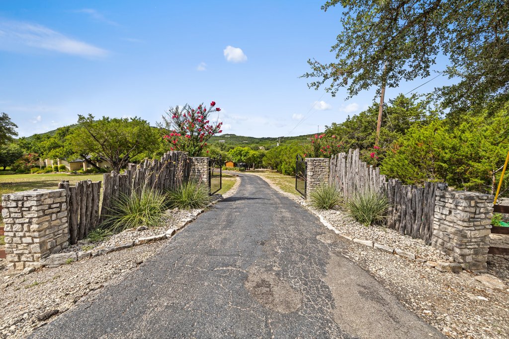 A private driveway entrance with rustic fencing and stone pillars leads to a secluded property nestled amongst rolling hills.