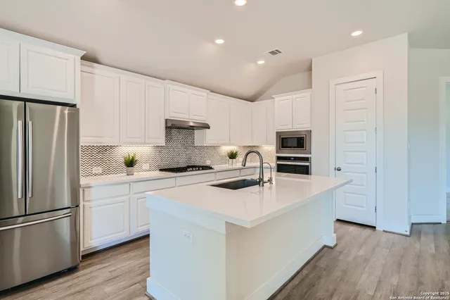 a kitchen with stainless steel appliances a sink stove refrigerator and white cabinets with wooden floor