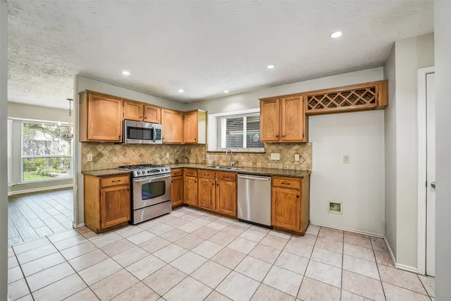 a large kitchen with stainless steel appliances granite countertop a stove top oven a sink dishwasher and a refrigerator with wooden cabinets