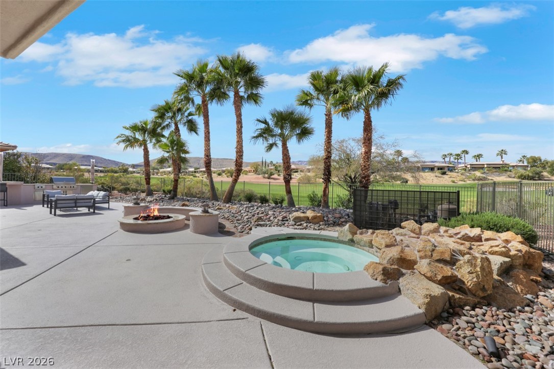 5015 Rivedro Street Las Vegas, NV 89135 - Photo 8 of 91 An inviting outdoor living space features a built-in spa, fire pit, and ample patio seating amidst lush palm trees and scenic golf course views.