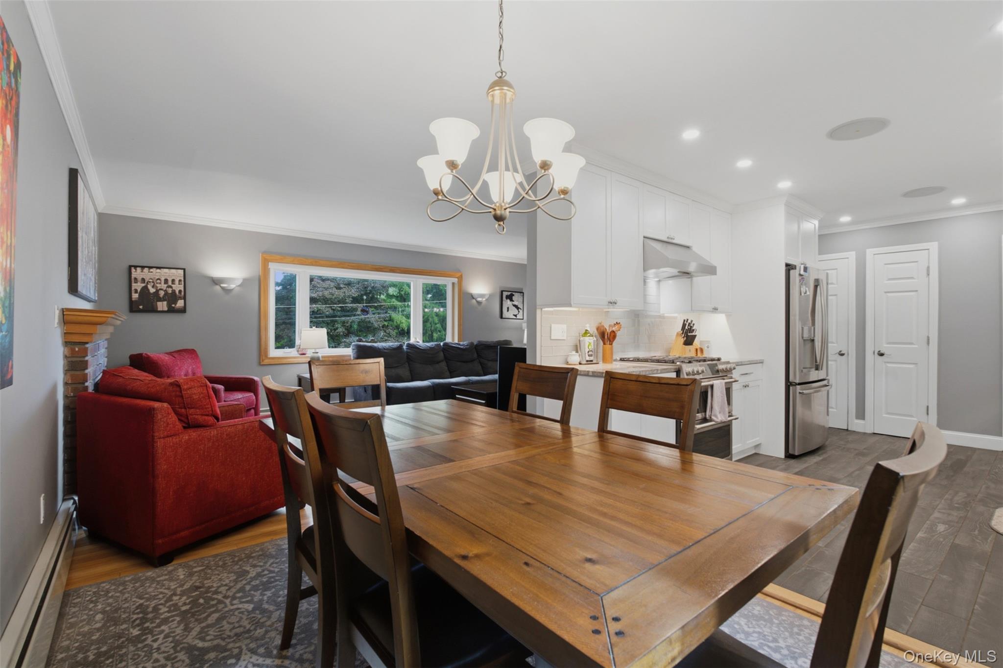 617 Cardinal Road Cortlandt Manor, NY 10567 - Photo 11 of 32 Open-concept living space featuring a dining area with a chandelier, a modern kitchen with white cabinetry and stainless steel appliances, and a living area with a large window and wall sconces