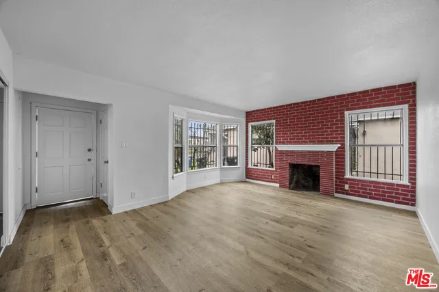 a view of an empty room with wooden floor fireplace and a window
