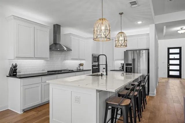a kitchen with stainless steel appliances granite countertop a sink a stove and chairs with wooden floor