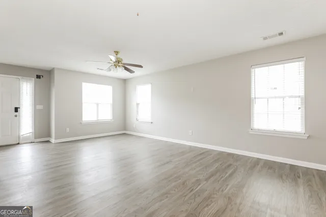 an empty room with wooden floor chandelier fan and windows