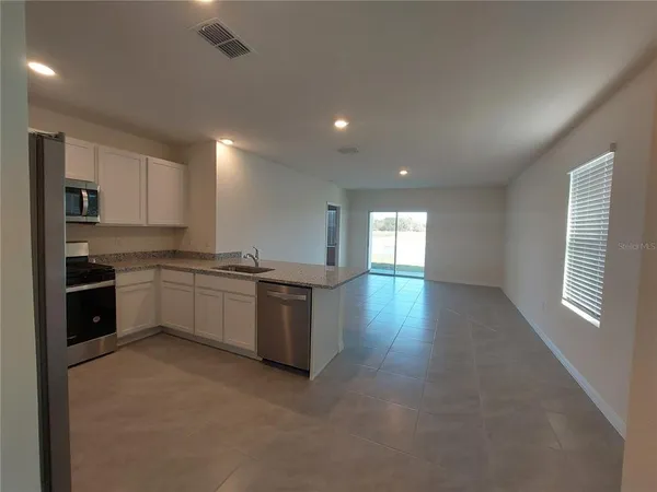 a large kitchen with stainless steel appliances granite countertop a stove a sink a refrigerator and white cabinets with wooden floor