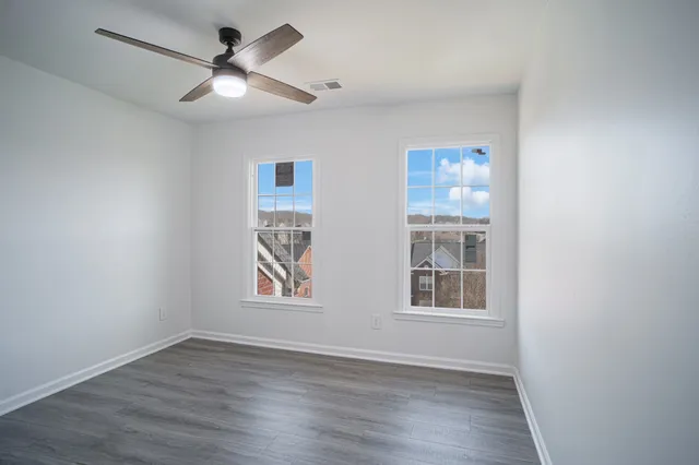 an empty room with wooden floor ceiling fan and windows