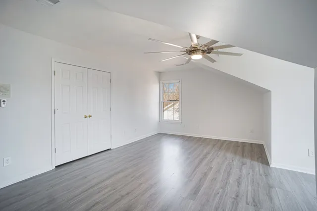 an empty room with wooden floor fan and windows