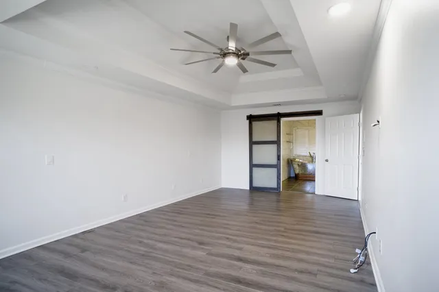 a view of an empty room with wooden floor and a ceiling fan