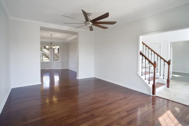 a view of an empty room with wooden floor and a ceiling fan