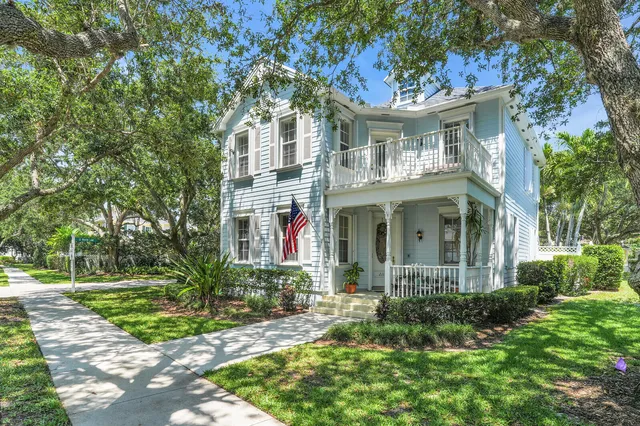 a view of a white house next to a yard with big trees