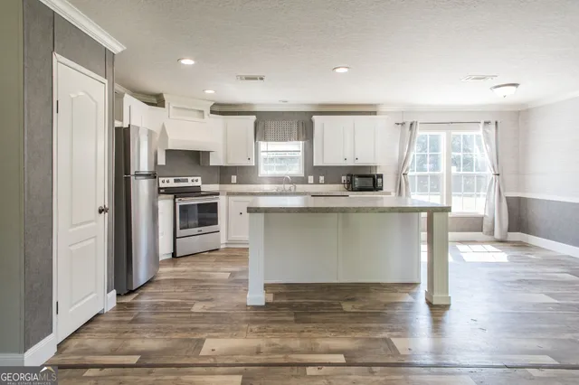 a kitchen with stainless steel appliances granite countertop a stove a sink dishwasher a refrigerator white cabinets and wooden floor