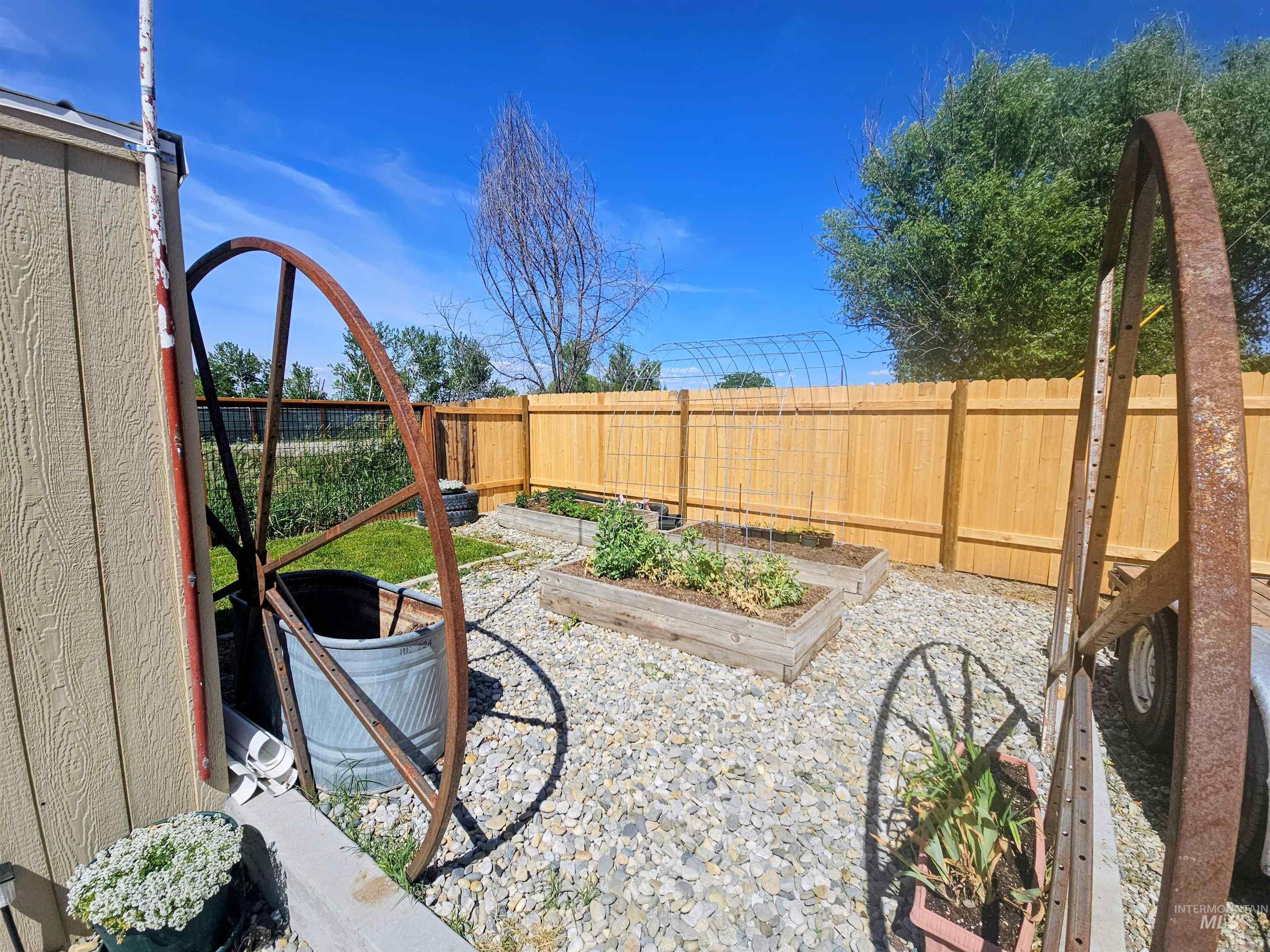 8392 Main Street Letha, ID 83636 - Photo 25 of 31 Gravel-covered backyard featuring a wooden privacy fence, two raised garden beds, and a metal arch structure