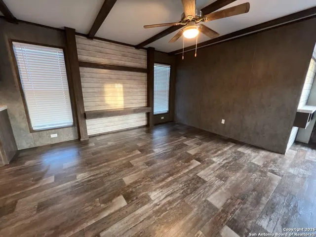 a view of an empty room with wooden floor and fan