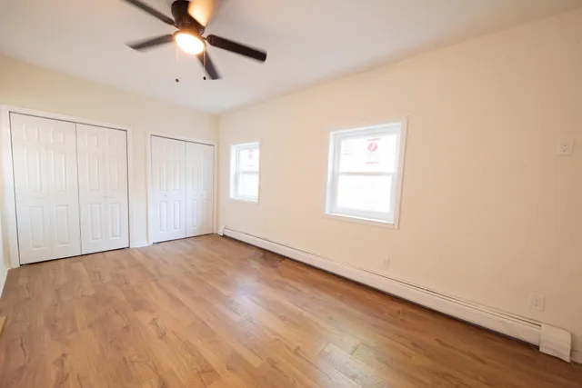 an empty room with wooden floor fan and windows