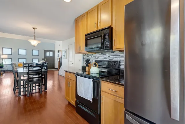 a kitchen with stainless steel appliances granite countertop a stove top oven a sink a dining table and chairs with wooden floor