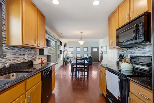 a kitchen with stainless steel appliances granite countertop a stove top oven a sink a dining table and chairs with wooden floor