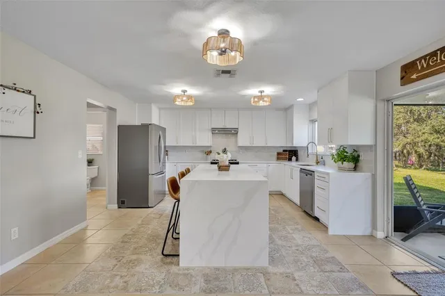a view of kitchen with stainless steel appliances kitchen island granite countertop a refrigerator oven a sink dishwasher and white cabinets with wooden floor
