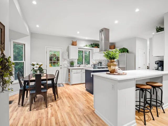 a kitchen with stainless steel appliances kitchen island granite countertop a stove a sink a refrigerator and white cabinets with wooden floor