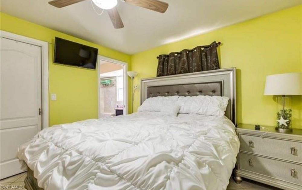5325 23rd Place Southwest Naples, FL 34116 - Photo 5 of 10 Bedroom featuring a ceiling fan, wall-mounted television, and an upholstered headboard