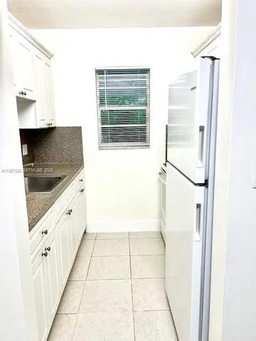 a large white kitchen with granite countertop a sink and a refrigerator