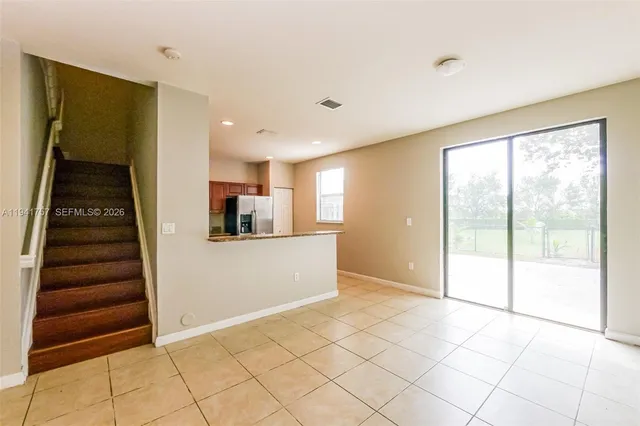 a view of an empty room with kitchen and entryway