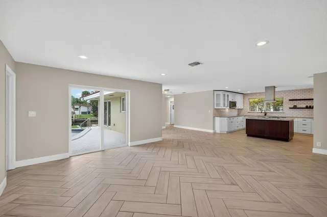 a view of an empty room with kitchen and window