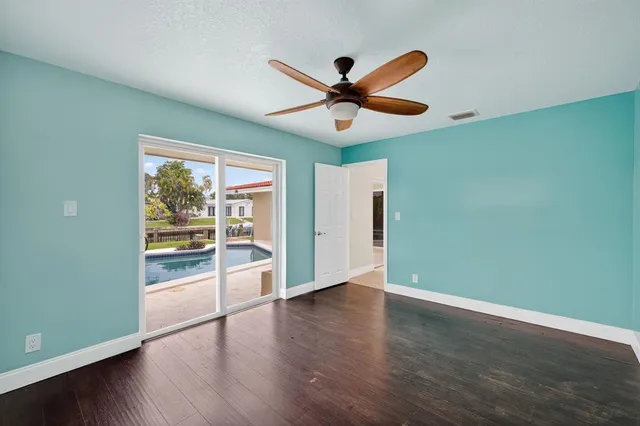 an empty room with wooden floor fan and windows
