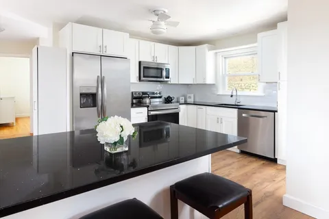 a kitchen with stainless steel appliances granite countertop a sink a stove a refrigerator cabinets and a dining table