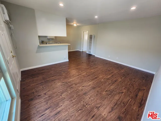 an empty room with wooden floor and a kitchen