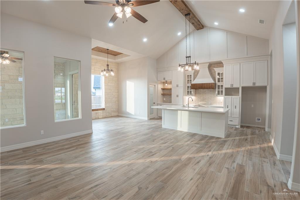 2618 Max Street Harlingen, TX 78552 - Photo 11 of 35 Bright open-concept living area featuring wood-finish flooring, a vaulted ceiling with exposed wood beam, a kitchen island with sink, white shaker cabinetry, and a stone accent wall