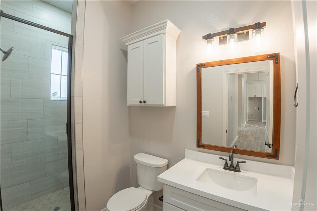 2618 Max Street Harlingen, TX 78552 - Photo 26 of 35 Bathroom featuring a glass-enclosed shower with tile surround, a single vanity with an undermount sink and quartz countertop, a wood-framed mirror, and a wall-mounted storage cabinet
