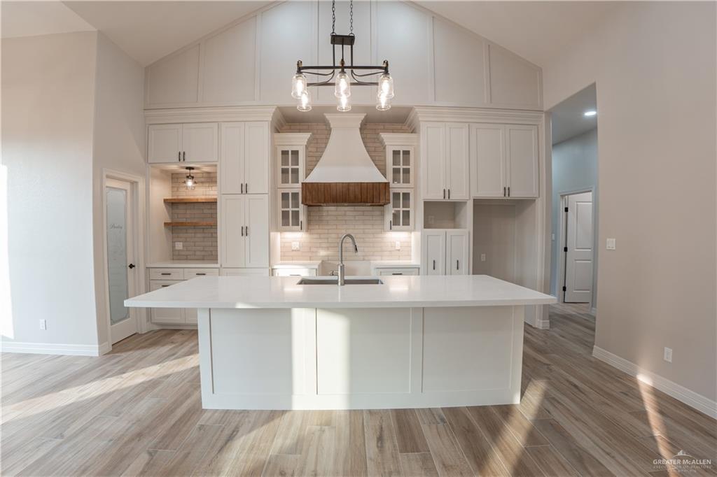 2618 Max Street Harlingen, TX 78552 - Photo 7 of 35 Kitchen featuring an expansive center island with an undermount sink, white cabinetry, wood-finish flooring, a vaulted ceiling with accent paneling, and an elegant chandelier