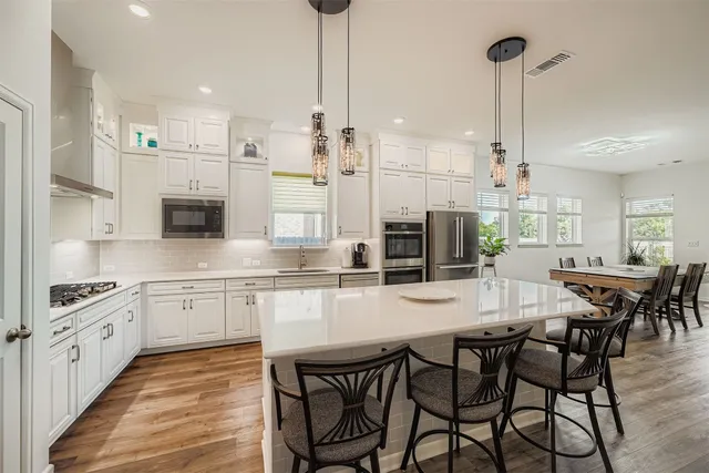 a kitchen with stainless steel appliances kitchen island granite countertop a dining table chairs stove and white cabinets