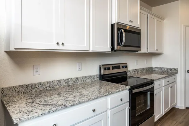 a kitchen with granite countertop white cabinets and a stove a oven with wooden floor