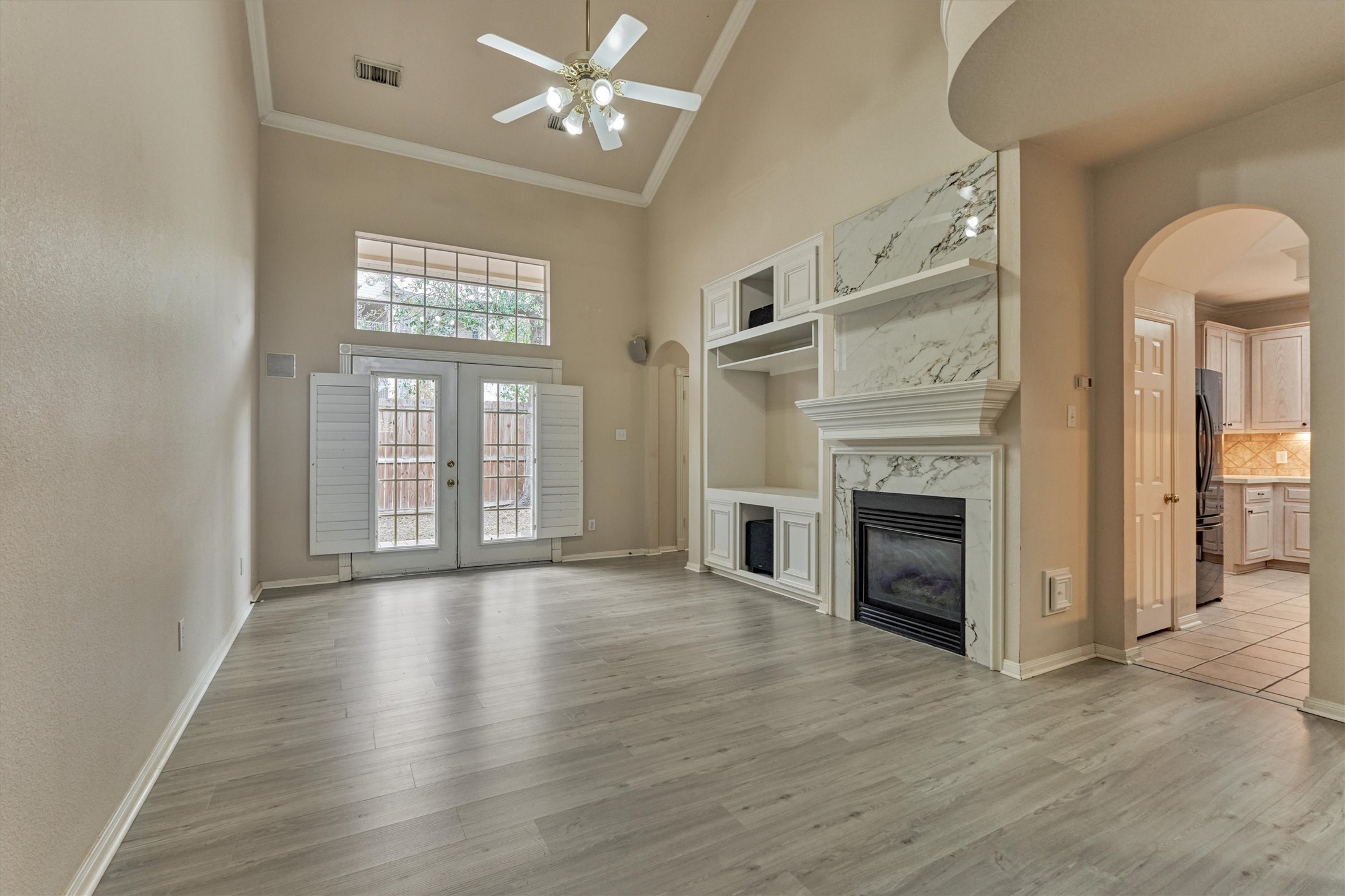 14420 Walters Road, Unit 26 Houston, TX 77014 - Photo 2 of 45 This spacious living room features high ceilings, a ceiling fan, and abundant natural light from large windows and French doors. It includes a stylish marble fireplace with built-in shelving and opens to a bright kitchen area through an arched entryway.