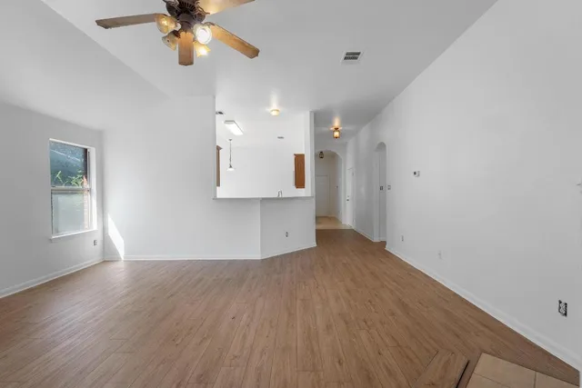 an empty room with wooden floor ceiling fan and windows
