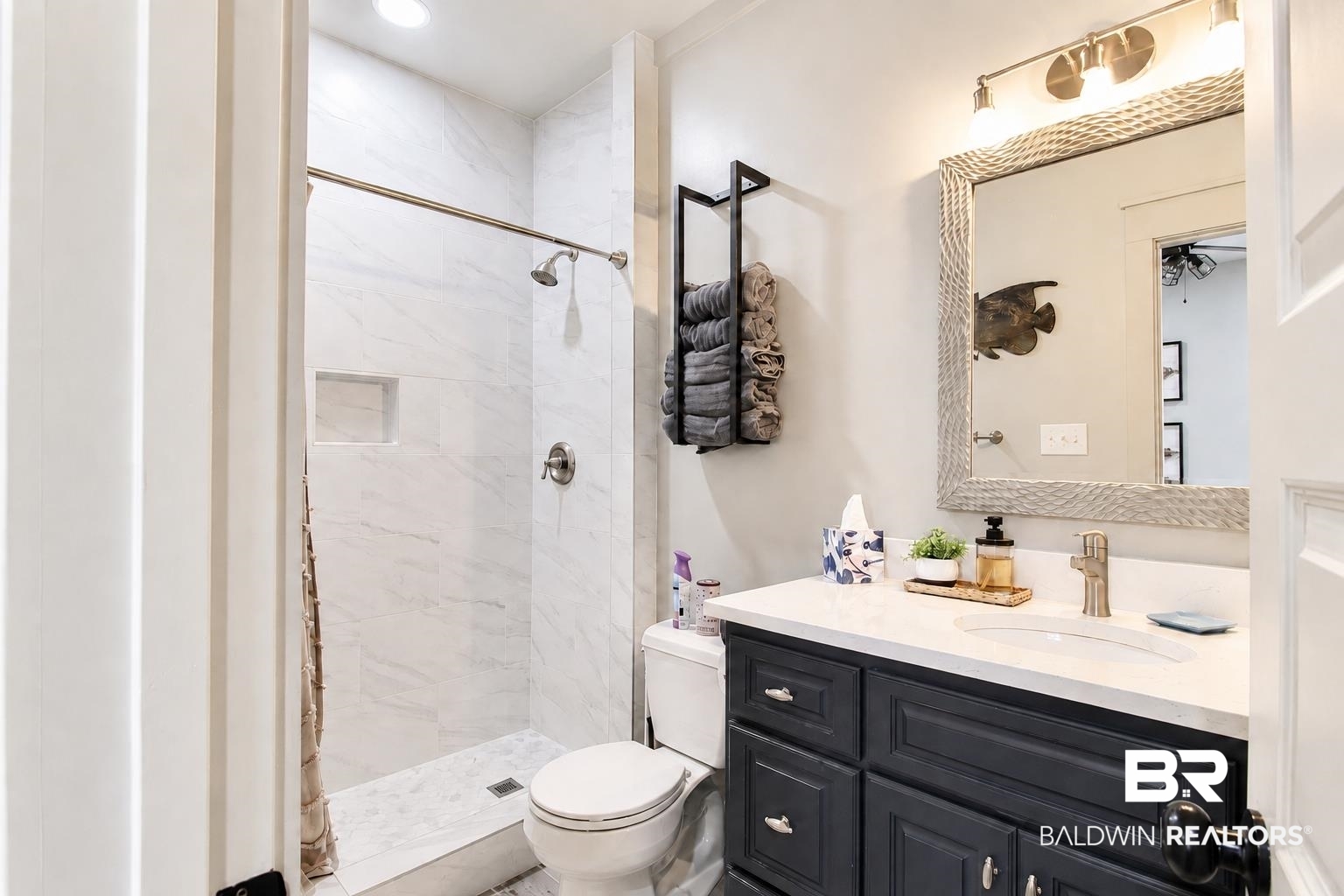 9825 Wolf Creek Ridge Elberta, AL 36530 - Photo 9 of 76 Full bathroom featuring a walk-in shower with marble-look tile surround and a built-in niche, a dark wood-finish vanity with a white countertop and integrated sink, and a framed mirror with a three-light vanity fixture