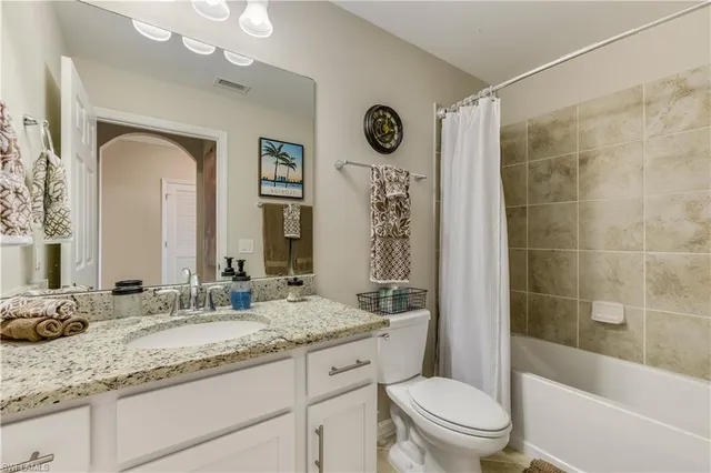 a bathroom with a granite countertop sink a toilet a mirror a vanity a bathtub and shower