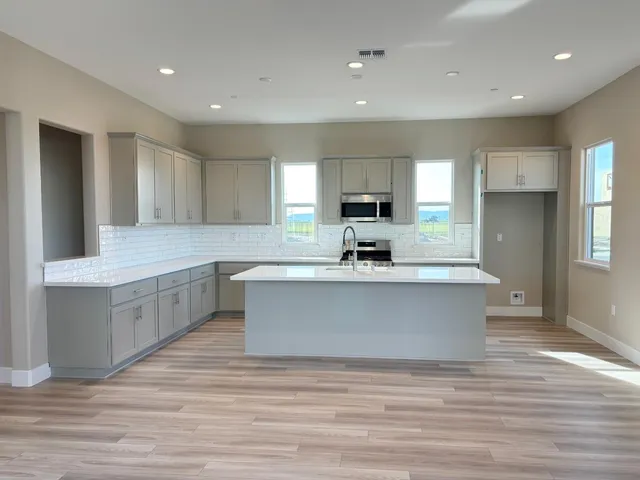 a large kitchen with kitchen island a sink dishwasher a stove a refrigerator and white cabinets with wooden floor