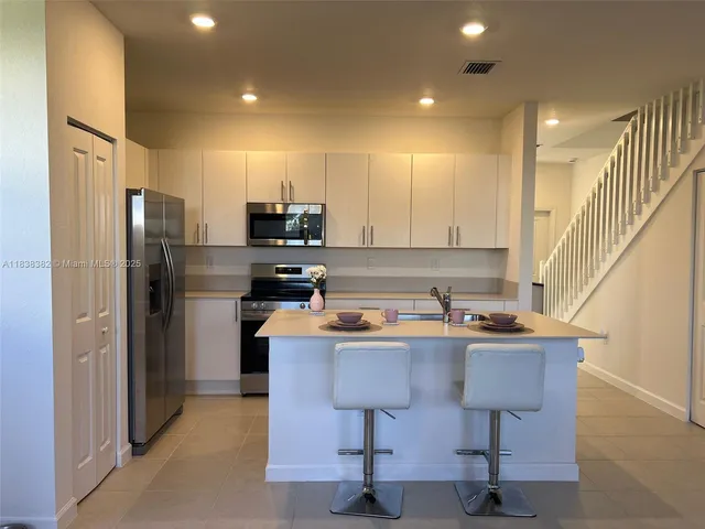 a kitchen with stainless steel appliances a refrigerator a stove a sink cabinets and a dining table with wooden floor