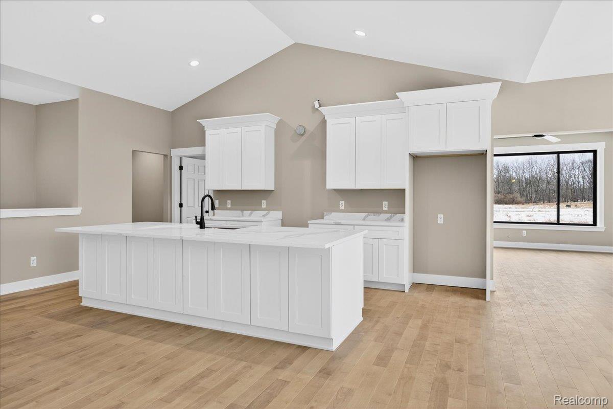 4050 Metamora Ridge Road Metamora, MI 48455 - Photo 32 of 65 Kitchen featuring a center island with sink, white cabinetry, light stone countertops, light wood-style floors, and high vaulted ceiling