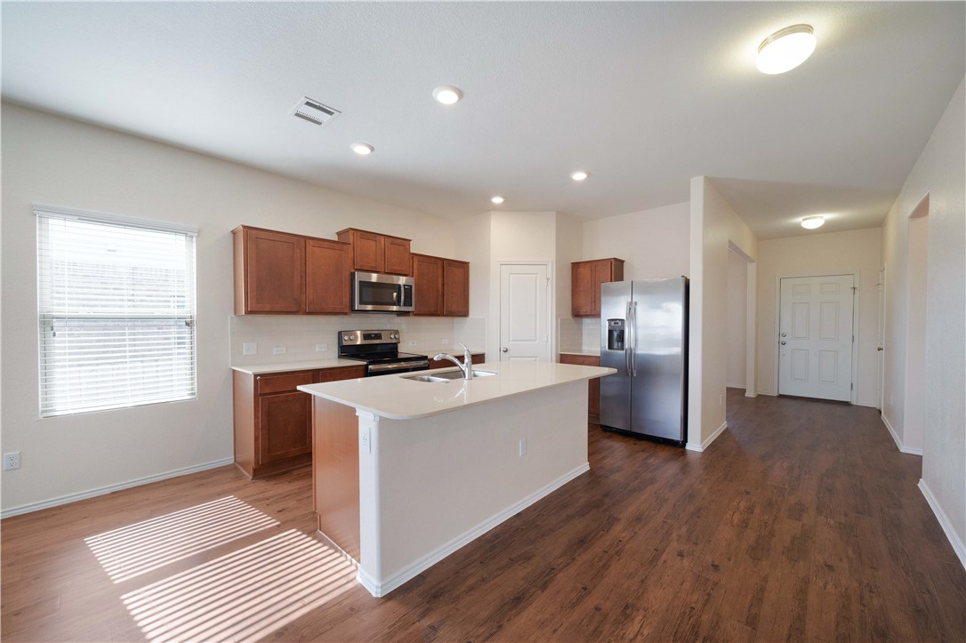 820 Kates Way Hutto, TX 78634 - Photo 11 of 30 a kitchen with stainless steel appliances a sink a stove a refrigerator cabinets and a wooden floor