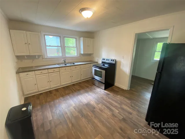 a large kitchen with granite countertop a refrigerator a sink dishwasher a stove and white countertops with wooden floor