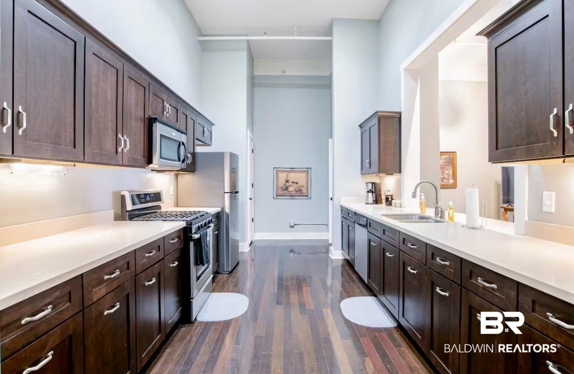 204 Conti Street, Unit 1C Mobile, AL 36602 - Photo 11 of 12 Kitchen featuring dark brown cabinets, appliances with stainless steel finishes, dark wood-type flooring, and light stone counters