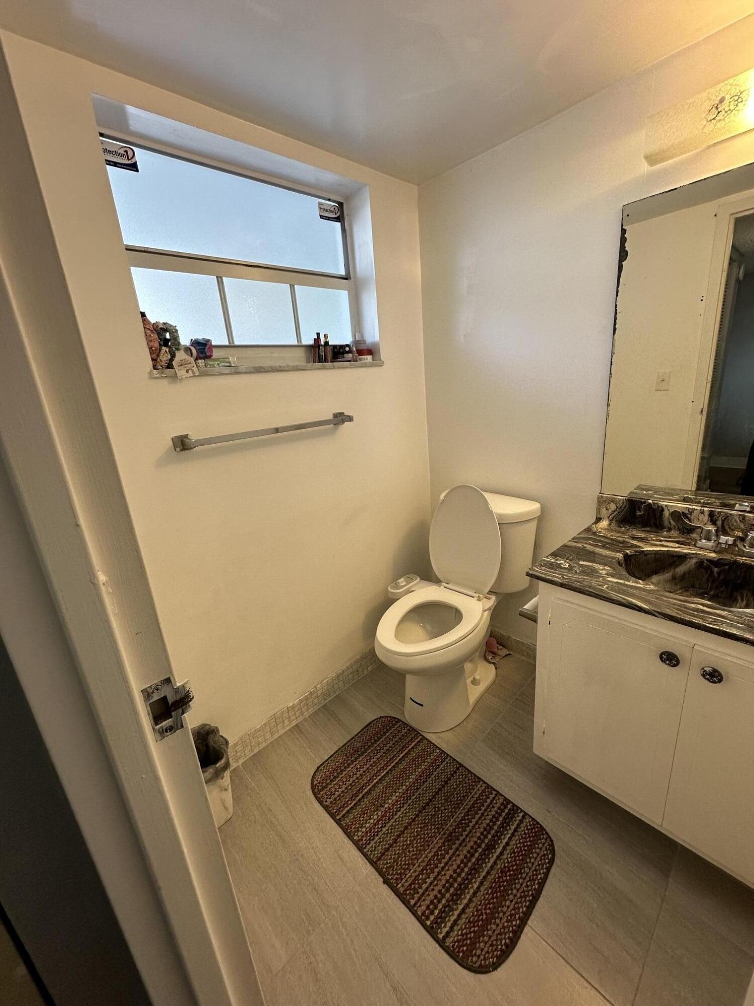 8341 Sands Point Boulevard, Unit B206 Tamarac, FL 33321 - Photo 5 of 11 a bathroom with a toilet a sink and mirror