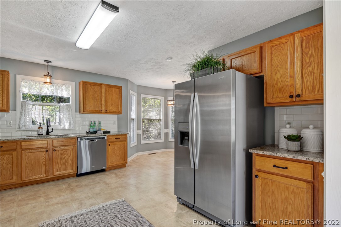 5823 Spreading Branch Road Hope Mills, NC 28348 - Photo 16 of 49 a kitchen with stainless steel appliances granite countertop a refrigerator a sink a stove with wooden cabinets and dining table